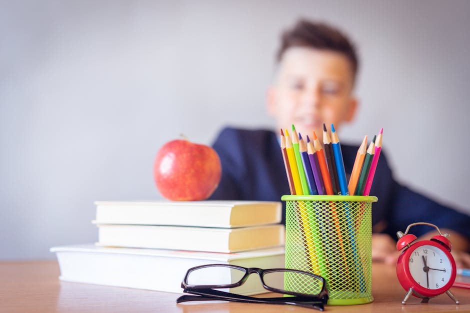 Schoolboy smiling behind a desk with books, pencils, and an alarm clock